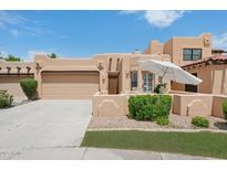 Beautiful home featuring a tan exterior, a two-car garage, and a charming front patio with an umbrella and chairs at 5756 N 78Th Pl, Scottsdale, AZ 85250