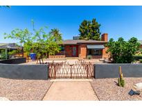 Charming red brick home with unique gate, desert landscaping, and mature trees under a bright blue sky at 1246 E Cambridge Ave, Phoenix, AZ 85006