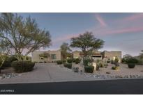 Stunning desert home featuring mature landscaping, gravel driveway, and ample curb appeal at twilight at 26049 N 104Th Pl, Scottsdale, AZ 85255