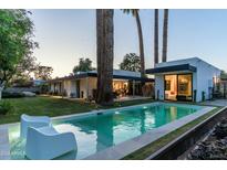 An inviting backyard pool features lounge chairs, a meticulously manicured lawn, and mature trees surrounding a modern home at 5311 E Mitchell Dr, Phoenix, AZ 85018