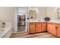Bright bathroom featuring a double sink vanity, soaking tub, and walk-in closet with ample storage at 9566 N 83Rd Dr, Peoria, AZ 85345