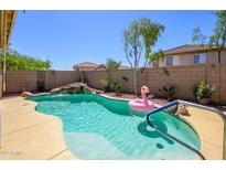 Backyard pool oasis featuring a waterfall and a playful pink flamingo float on a sunny day at 22783 W Cantilever St, Buckeye, AZ 85326