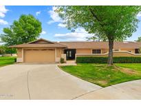 Single-story home featuring an attached two-car garage, manicured lawn and mature trees under a sunny sky at 19053 N Lakeforest Dr, Sun City, AZ 85373