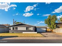 Charming single-story home features a dark gray facade, white trim, desert landscaping, and detached garage at 4518 W Rose Ln, Glendale, AZ 85301
