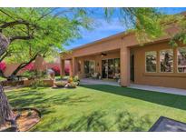 View of a landscaped backyard with synthetic grass, covered patio, grill, and green trees at 13914 E Laurel Ln, Scottsdale, AZ 85259