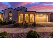 Charming home exterior features arched entryway, desert landscaping, and warm lighting against a colorful dusk sky at 5228 S 106Th Pl, Mesa, AZ 85212