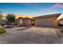 Charming single-story home with a well-maintained lawn and two-car garage at sunset at 22977 E Desert Spoon Dr, Queen Creek, AZ 85142