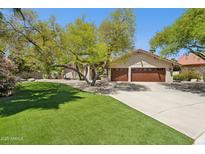 Charming single-story home featuring lush landscaping, green grass, mature trees and a two-car garage at 7508 E Aster Dr, Scottsdale, AZ 85260