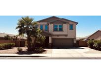 Two-story tan house featuring a two-car garage, desert landscaping, and palm trees at 41143 W Rio Bravo Dr, Maricopa, AZ 85138