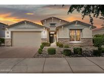 Charming single-story home featuring a two-car garage, stone accents, and meticulously landscaped front yard at sunset at 9510 E Theia Dr, Mesa, AZ 85212