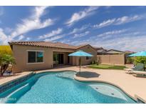 Inviting backyard pool with turquoise water, putting green, and blue patio umbrella at 2701 N Black Rock Rd, Buckeye, AZ 85396