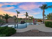 Stunning pool with rock waterfall feature, surrounded by lush landscaping and mature palm trees at sunset at 18822 E Flintlock Dr, Queen Creek, AZ 85142