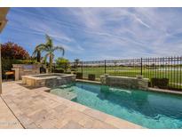 Beautiful pool and spa with a stone waterfall feature overlook a golf course with an outdoor kitchen area at 36298 N Crucillo Dr, Queen Creek, AZ 85140