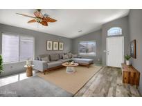 Bright living room featuring a large gray sofa, hardwood floors, and a decorative ceiling fan at 13416 W Ventura St, Surprise, AZ 85379