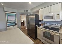 Bright kitchen with stainless steel appliances, white cabinets, and a view into a room with a piano at 1904 E Jarvis Ave, Mesa, AZ 85204
