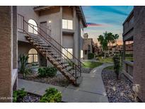 A well-maintained condo exterior features classic desert landscaping, with walkways and exterior stairs visible at sunset at 930 N Mesa Dr # 1079, Mesa, AZ 85201