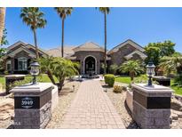 Gorgeous single-story stone home with a brick walkway, fountain, well-manicured landscaping, and towering palm trees at 3949 E Norcroft Cir, Mesa, AZ 85215