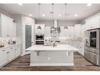 A bright kitchen boasts white cabinets, stainless appliances, a large island, and stylish backsplash at 10949 N 183Rd Dr, Surprise, AZ 85388