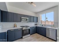 Modern kitchen with stainless steel appliances, blue cabinets, white countertops, and a stylish tile backsplash at 3233 E Sequoia Dr, Phoenix, AZ 85050