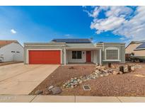 Charming single-story home showcasing desert landscaping, a red garage door, and solar panels under a bright sky at 6038 W Gelding Dr, Glendale, AZ 85306