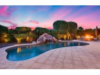 Beautiful pool featuring a rock waterfall and lush landscaping, perfect for relaxing evenings at 19414 W Pasadena Ave, Litchfield Park, AZ 85340