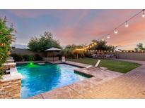 Inviting backyard pool with lounge chairs, lush landscaping, and an outdoor fireplace illuminated by string lights at 5424 N 186Th Dr, Litchfield Park, AZ 85340