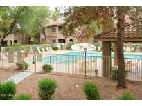 Community pool area with lounge chairs and tables, surrounded by mature landscaping and a wrought iron fence at 15252 N 100Th St # 1172, Scottsdale, AZ 85260