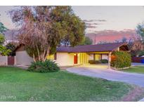 Charming single-story home with a circular driveway, lush greenery, and a vibrant red front door at 645 S Esquire Way, Mesa, AZ 85202