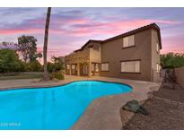 Backyard pool with stone surround against the backdrop of a two-story home with a covered patio and vibrant sunset at 704 E Gemini Pl, Chandler, AZ 85249