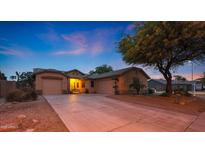 Charming home featuring three-car garage and inviting curb appeal with a mature shade tree at dusk at 15245 W Crocus Dr, Surprise, AZ 85379