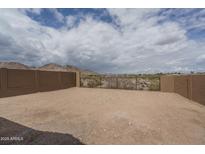 Desert backyard featuring a brick wall and metal gate with mountain views under a partly cloudy sky at 2823 N 212Th Dr, Buckeye, AZ 85396