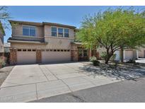 Two-story home featuring a three-car garage, desert landscaping, and a mature shade tree in the front yard at 30263 W Crittenden Ln, Buckeye, AZ 85396