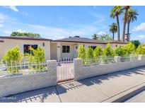 Beige home with a white picket fence, mature landscaping, and large green palm trees at 701 W Windsor Ave, Phoenix, AZ 85007