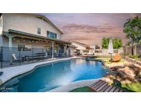 Inviting backyard pool with rock features, a safety fence, patio, and lovely landscaping at 7931 W Harmony Ln, Peoria, AZ 85382