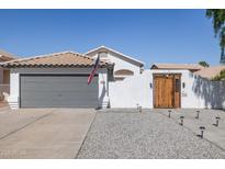 Charming home featuring a gray garage door, a wooden gate, and desert landscaping at 13320 N 82Nd Dr, Peoria, AZ 85381