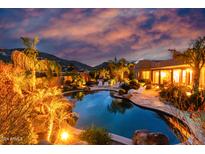 Backyard features a custom pool, rock waterfall, and lush desert landscaping with mountain views at sunset at 2731 W Desert Ranch Rd, Phoenix, AZ 85086