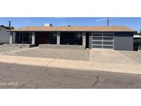 Charming single-story home with a modern grey exterior, stone landscaping, and a transparent glass garage door at 8520 E Mackenzie Dr, Scottsdale, AZ 85251