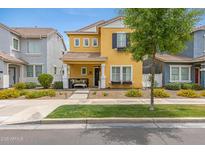 Charming two-story home featuring a yellow facade, manicured landscaping, and a welcoming front porch with seating at 1316 S Minneola Ln, Gilbert, AZ 85296