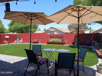 Inviting backyard featuring artificial grass, seating under umbrellas, a red brick wall, and well-kept landscaping at 14211 N 149Th Dr, Surprise, AZ 85379