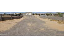 Gravel driveway leading to a gated property with metal buildings, enclosed by concrete fencing with wrought iron toppers at 30940 N Varnum Rd, San Tan Valley, AZ 85143