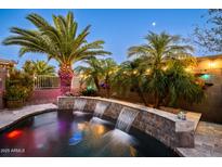 A lush backyard highlighting a beautiful pool with a triple waterfall feature surrounded by palms at 42293 W Good Vibrations Ln, Maricopa, AZ 85138