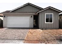 Charming single-story home with gray siding, brick driveway, a white garage door, and well-manicured landscaping at 18165 W Larkspur Dr, Goodyear, AZ 85338