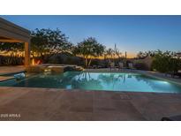 Beautifully lit backyard pool area with a spa, lounge chairs, and lush desert landscaping at dusk at 8248 E Arroyo Hondo Rd, Scottsdale, AZ 85266