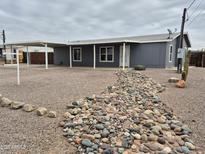 Charming single-story home with a covered carport, grey siding, and a decorative rock garden at 329 N 83Rd Pl, Mesa, AZ 85207