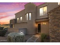 Inviting home exterior featuring a stone accent wall, desert landscaping, and soft illumination at dusk at 19475 N Grayhawk Dr # 1115, Scottsdale, AZ 85255