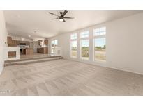 Bright living room featuring neutral carpet, ceiling fan, and a series of windows overlooking the outdoor space at 13217 S Tuthill Rd, Buckeye, AZ 85326