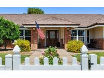 Charming home entrance with brick accents, American flag, mature landscaping, and white picket fence at 3160 E Fox St, Mesa, AZ 85213