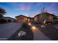 Charming home exterior with a paved walkway, desert landscaping, and warm lighting at dusk at 19334 W Pasadena Ave, Litchfield Park, AZ 85340