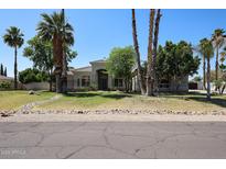 Charming single-story home featuring a well-manicured lawn and desert landscaping, complemented by mature palm trees at 12721 W Georgia Ave, Litchfield Park, AZ 85340