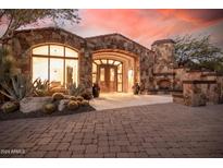 Close up of a stone home featuring an outdoor fireplace and arched entry with double wooden doors at 7552 E Whisper Rock Trl, Scottsdale, AZ 85266
